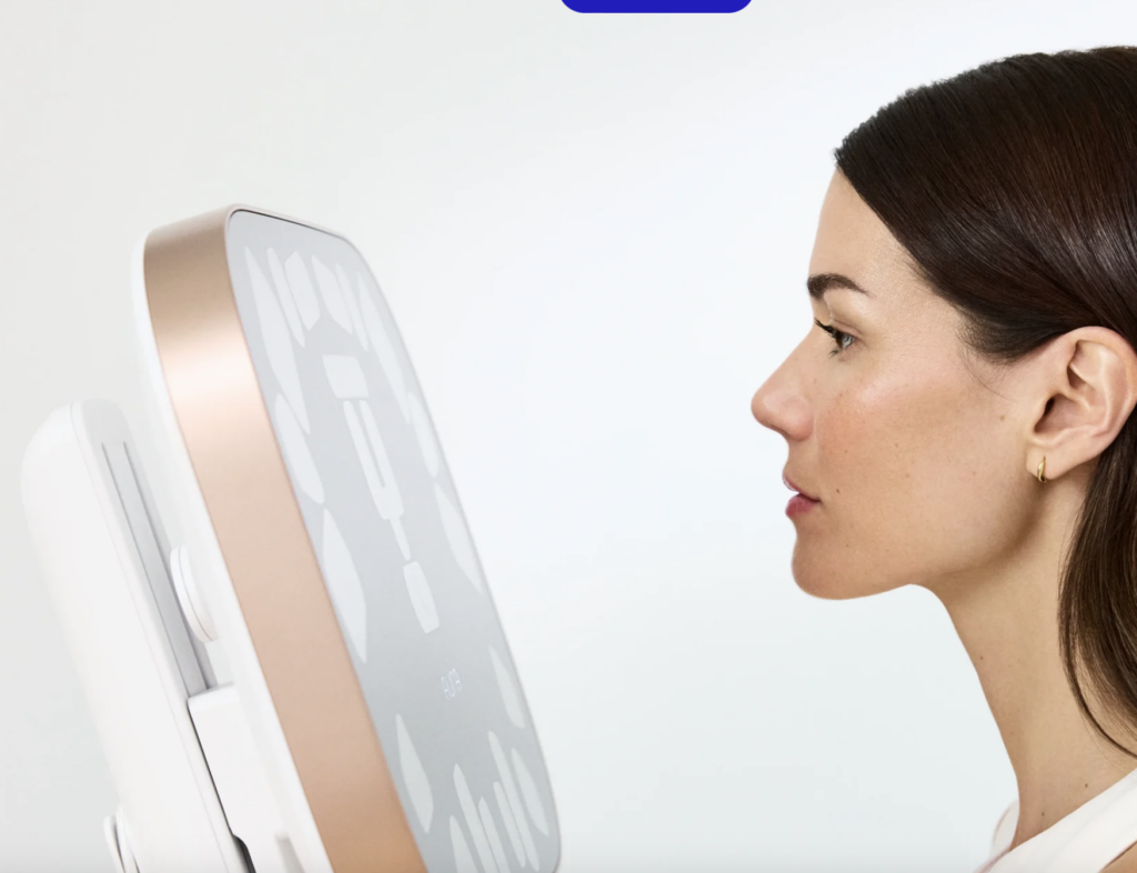 Profile view of a woman facing a modern digital scale with a large touchscreen display in rose-gold framing.