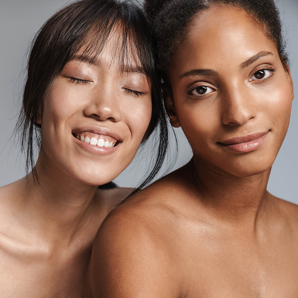 Two women pose closely: one smiles with eyes closed, the other looks at the camera.