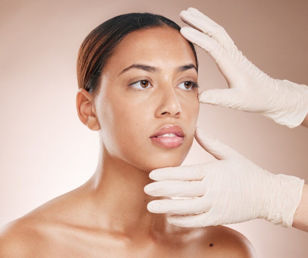 Gentle facial examination with gloved hands touching the woman's forehead and jawline.